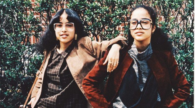 This color photograph shows identical twins wearing
popular fashion from the 1980s in the East Flatbush section of Brooklyn, New York, in 1980. The girls are wearing oversized coats, skirts, shirts, and Cazal glasses. (Photo by Jamel Shabazz, courtesy National Museum of African American History and Culture)